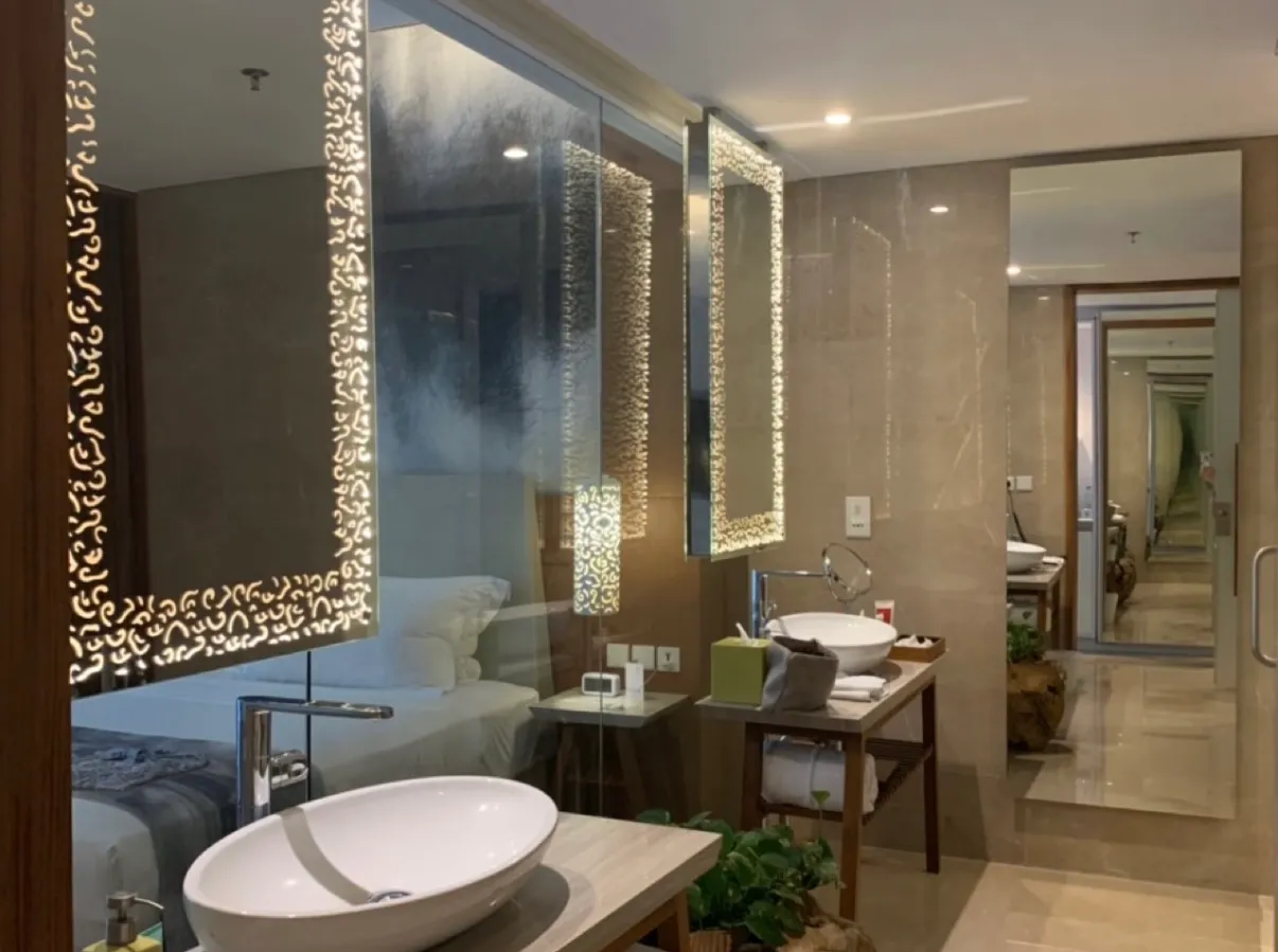 A Maya Sanur bathroom with vessel basins under backlit mirrors, open to the bedroom through glass