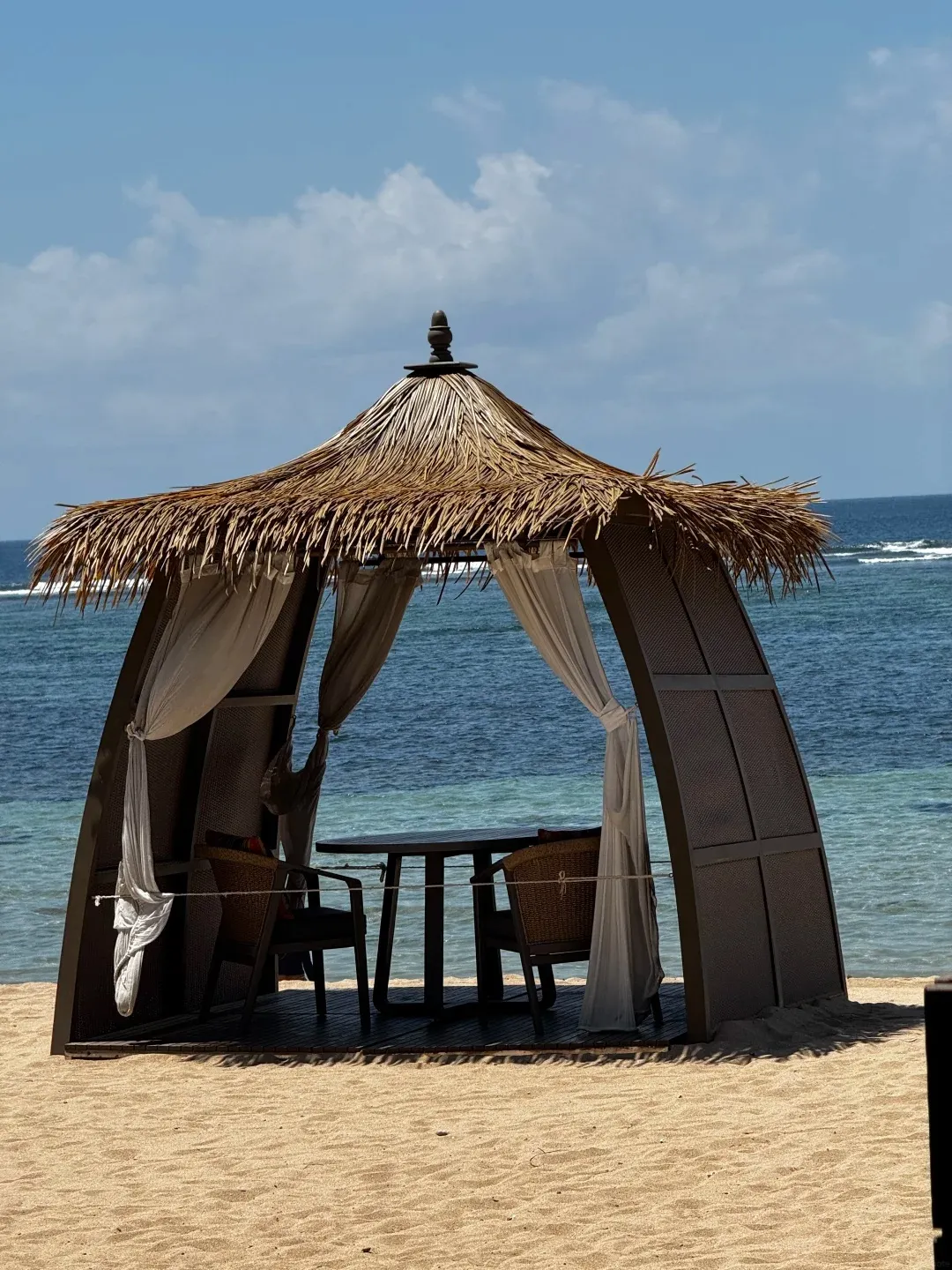 A thatched beach cabana with a table set on the sand