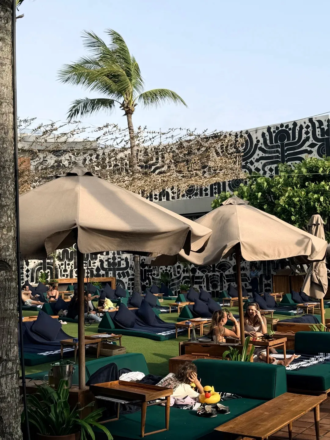 Canvas umbrellas over the beach club lawn, with people lounging on green daybeds