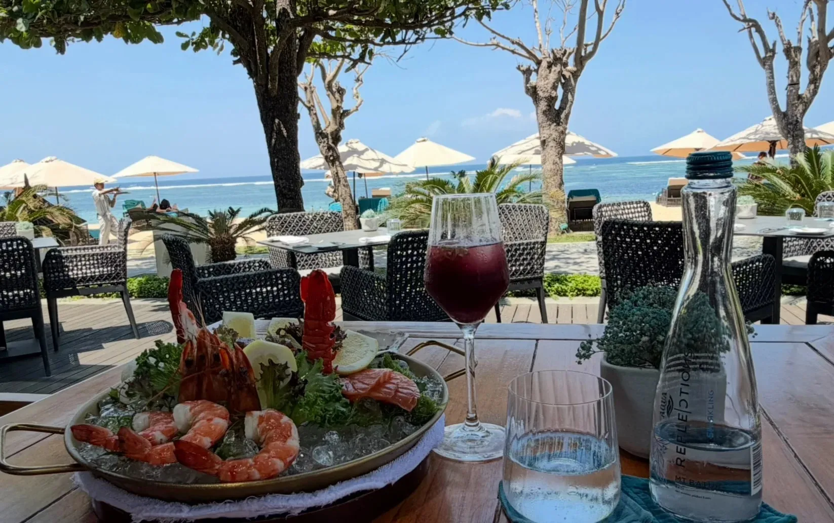 A seafood platter and sangria at a beachfront table, with umbrellas on the sand behind