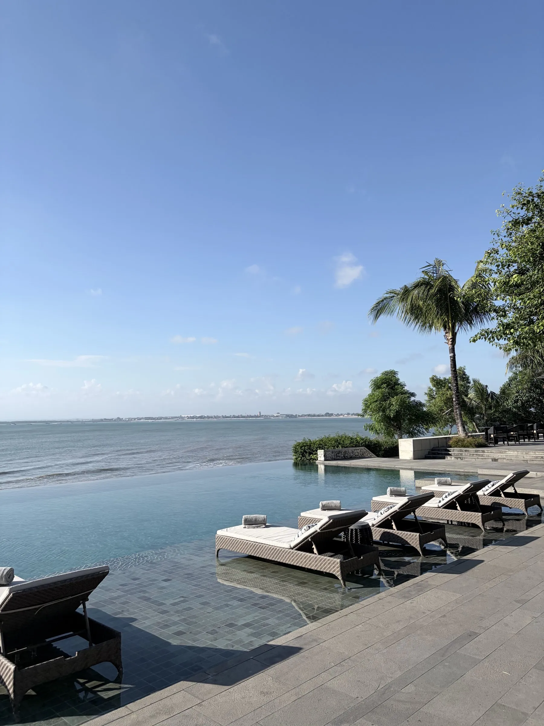 The lap pool by the beach, with loungers set in the shallow edge and the bay stretching beyond