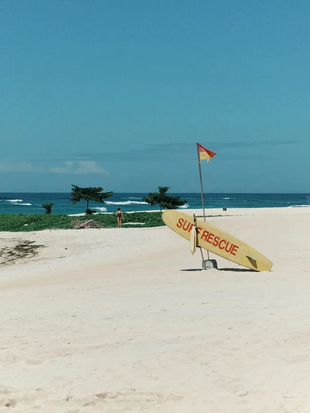A yellow surf rescue board on white sand by the water