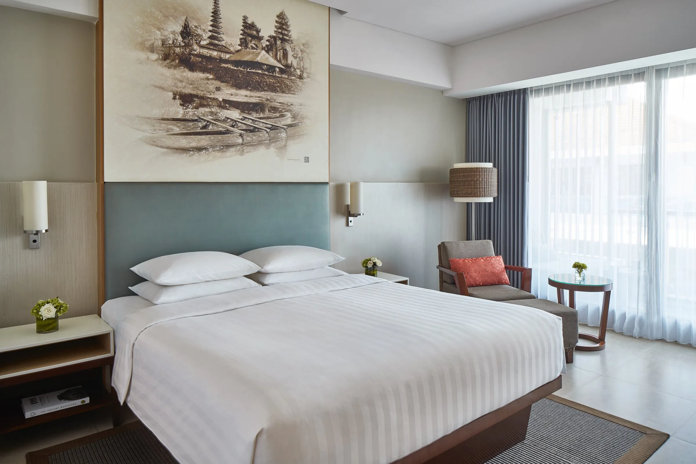 A Courtyard Seminyak bedroom with a king bed, a temple sketch above the headboard and an armchair by the window