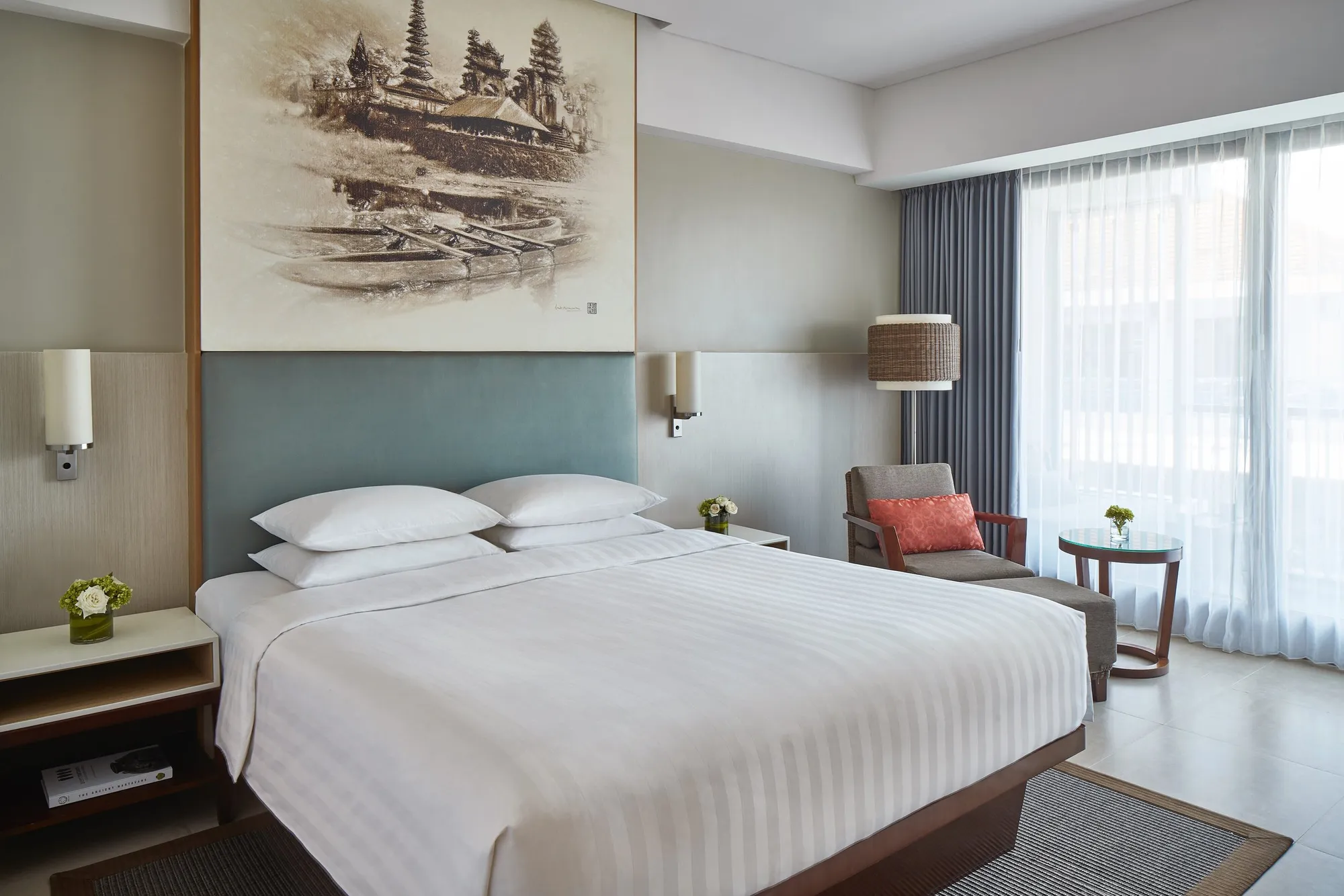 A Courtyard Seminyak bedroom with a king bed, a temple sketch above the headboard and an armchair by the window