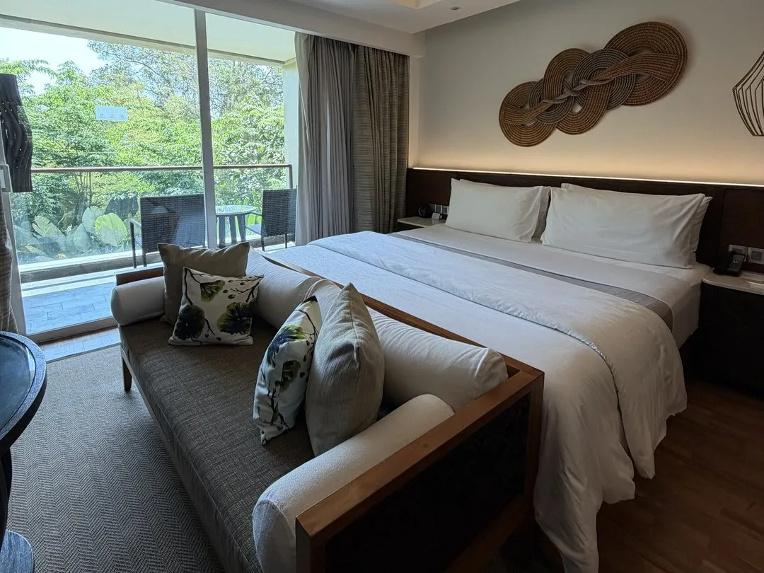 A Westin Ubud bedroom with a king bed, a daybed sofa at its foot and glass doors onto a jungle-view balcony
