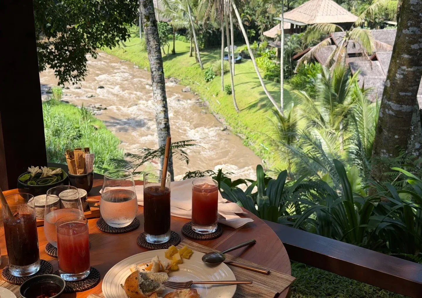 Breakfast juices and pastries on a table above the river, with rice paddies beyond