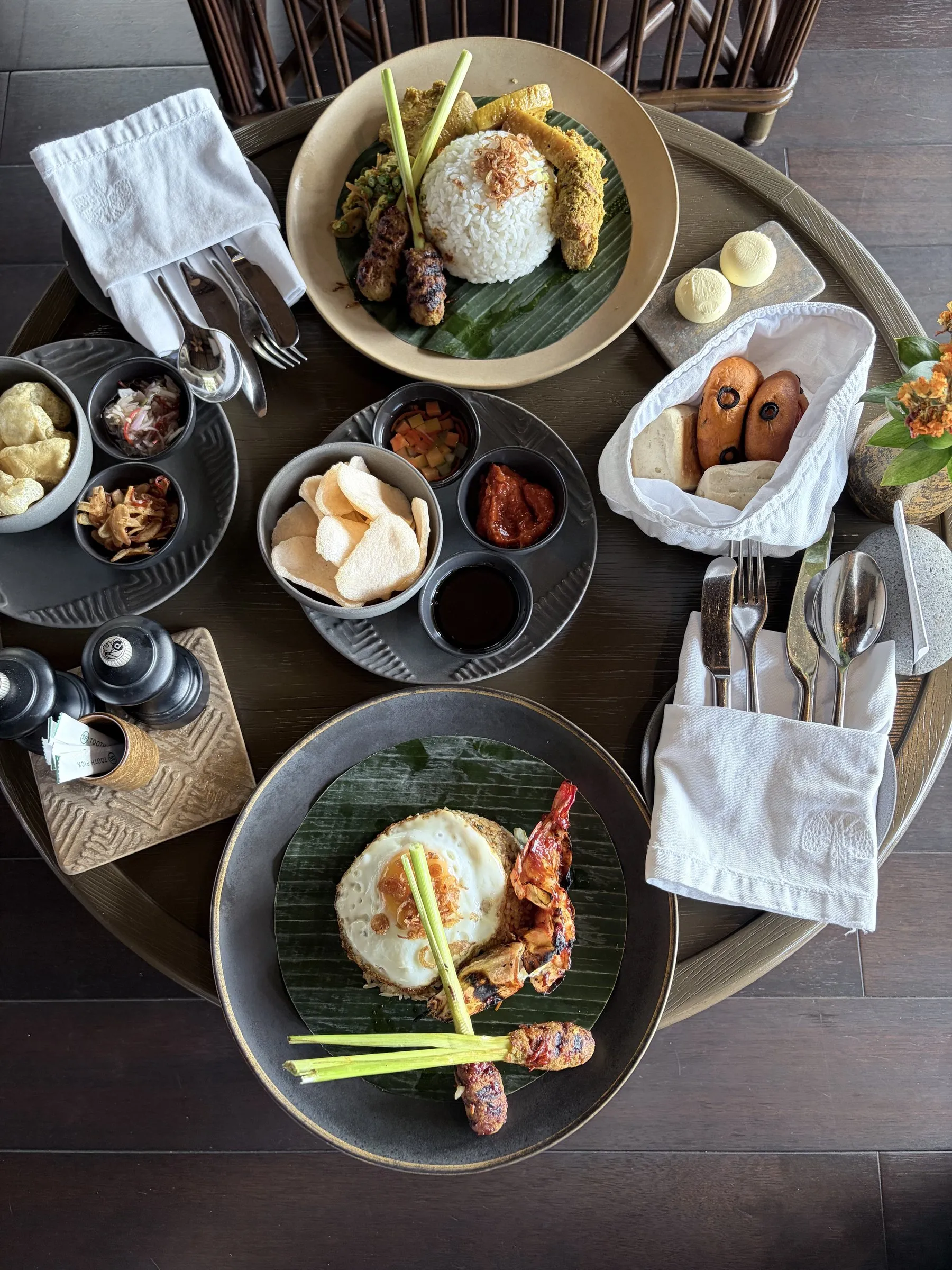 An Indonesian breakfast for two from above, with fried eggs, satay on banana leaves, sambals and crackers