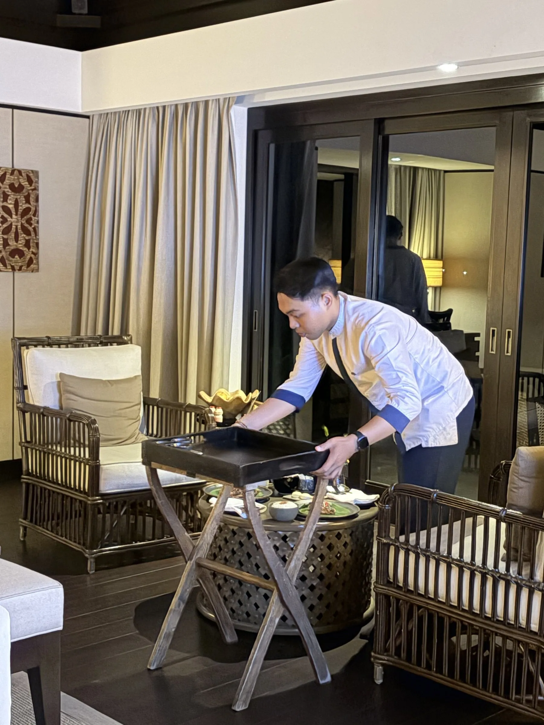 A butler setting a breakfast tray on a stand in a villa living room