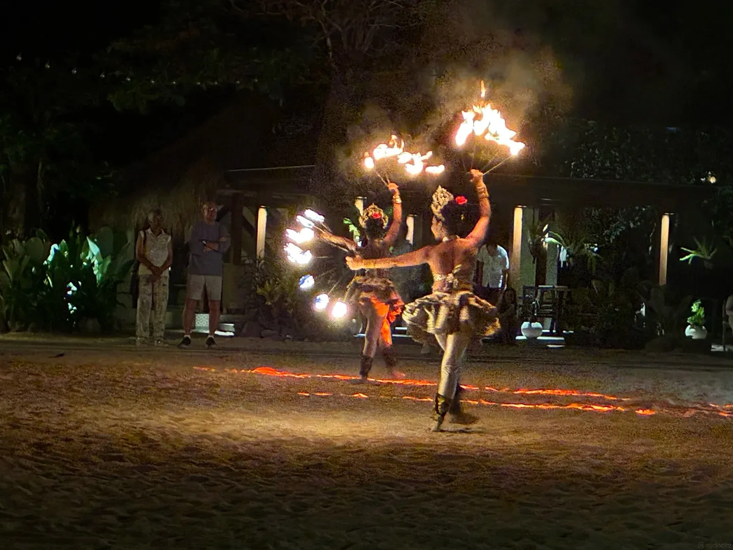 A fire dancer spinning flames on the sand at night