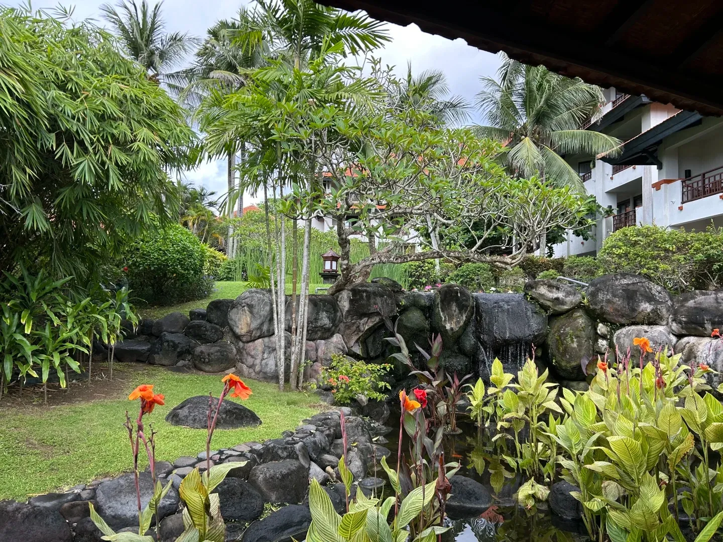 Canna lilies around a rock pond and small waterfall in the gardens, with guest wings behind
