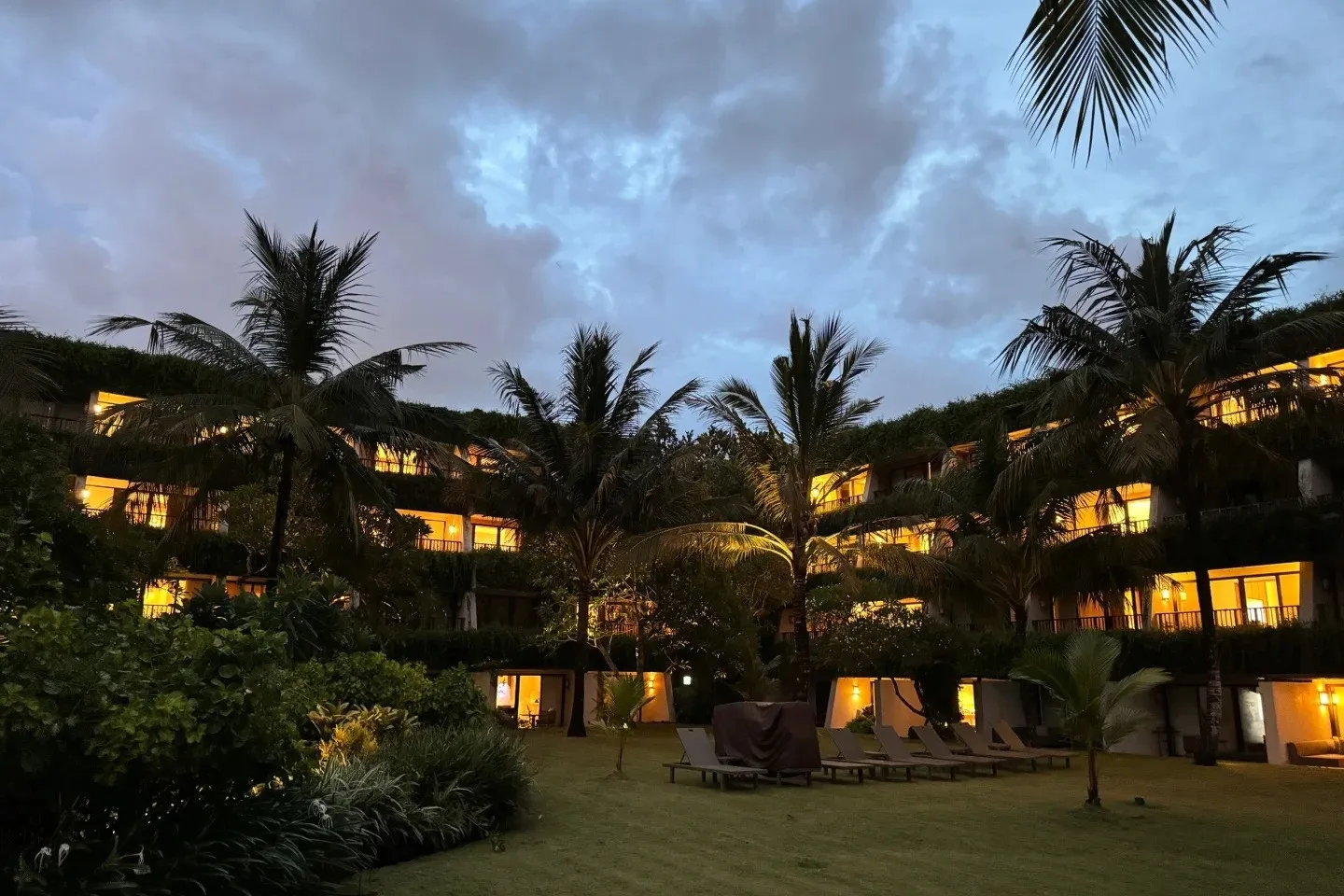 Guest wings lit up at dusk behind a lawn and coconut palms