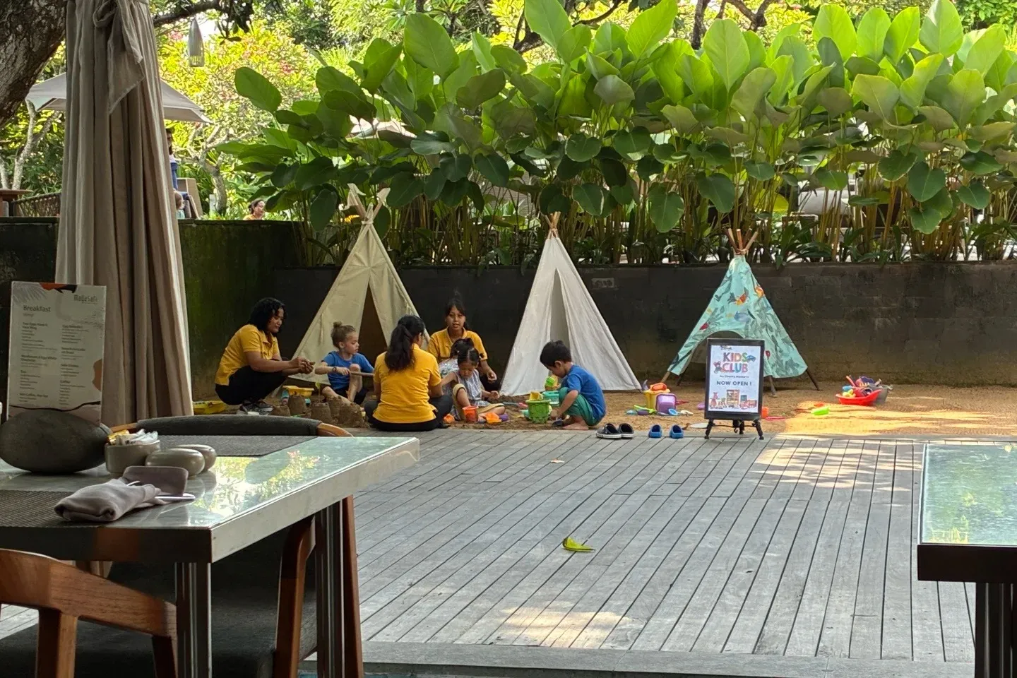 Kids building sandcastles with staff by small teepees at the Maya Sanur kids club