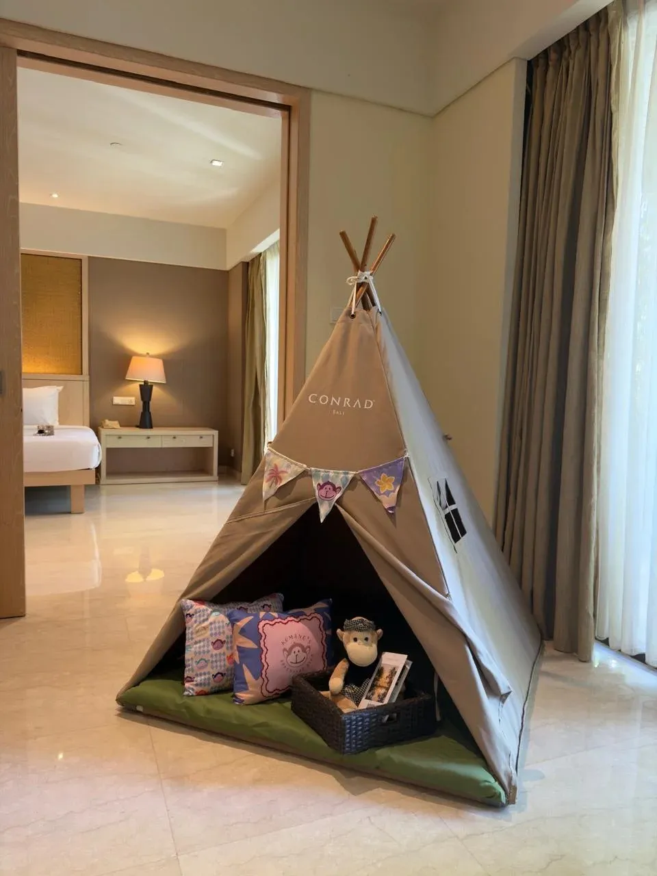 A Conrad-branded play tent with cushions and a toy monkey set up in a guest room