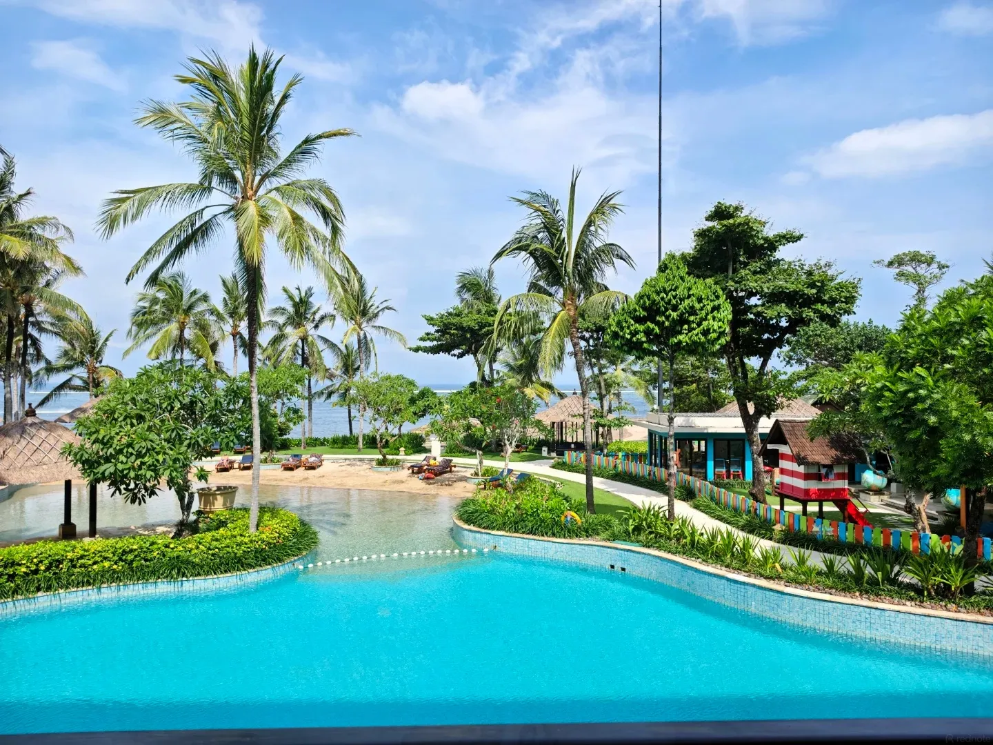 A curving lagoon pool between palm-shaded islands, with the sea behind