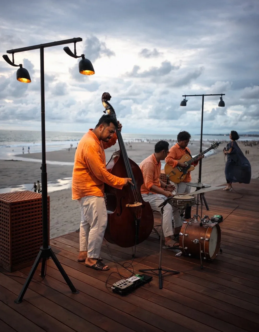 A band playing double bass and guitar on a deck by the beach at sunset