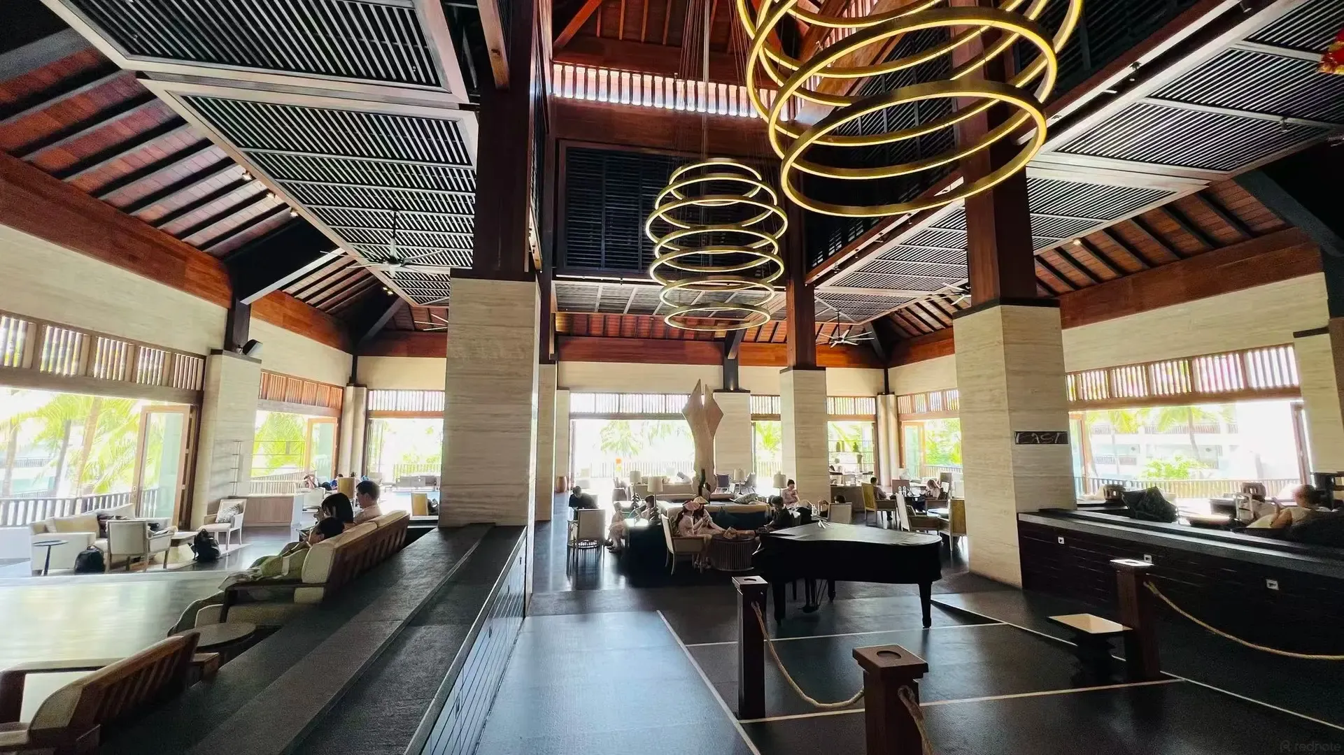 The lobby lounge under a timber roof, with a piano and ring chandeliers