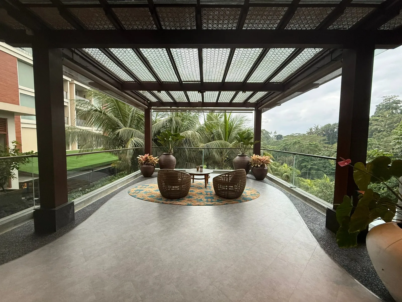 A covered lounge terrace with wicker chairs, looking out over palms and the valley