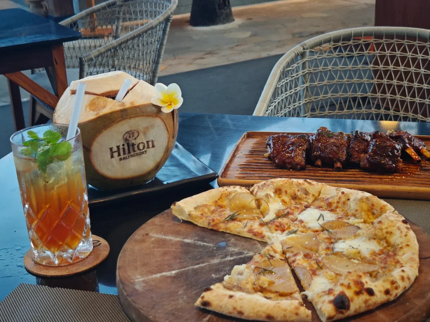 Pizza, ribs, iced tea and a branded coconut at a beachside table