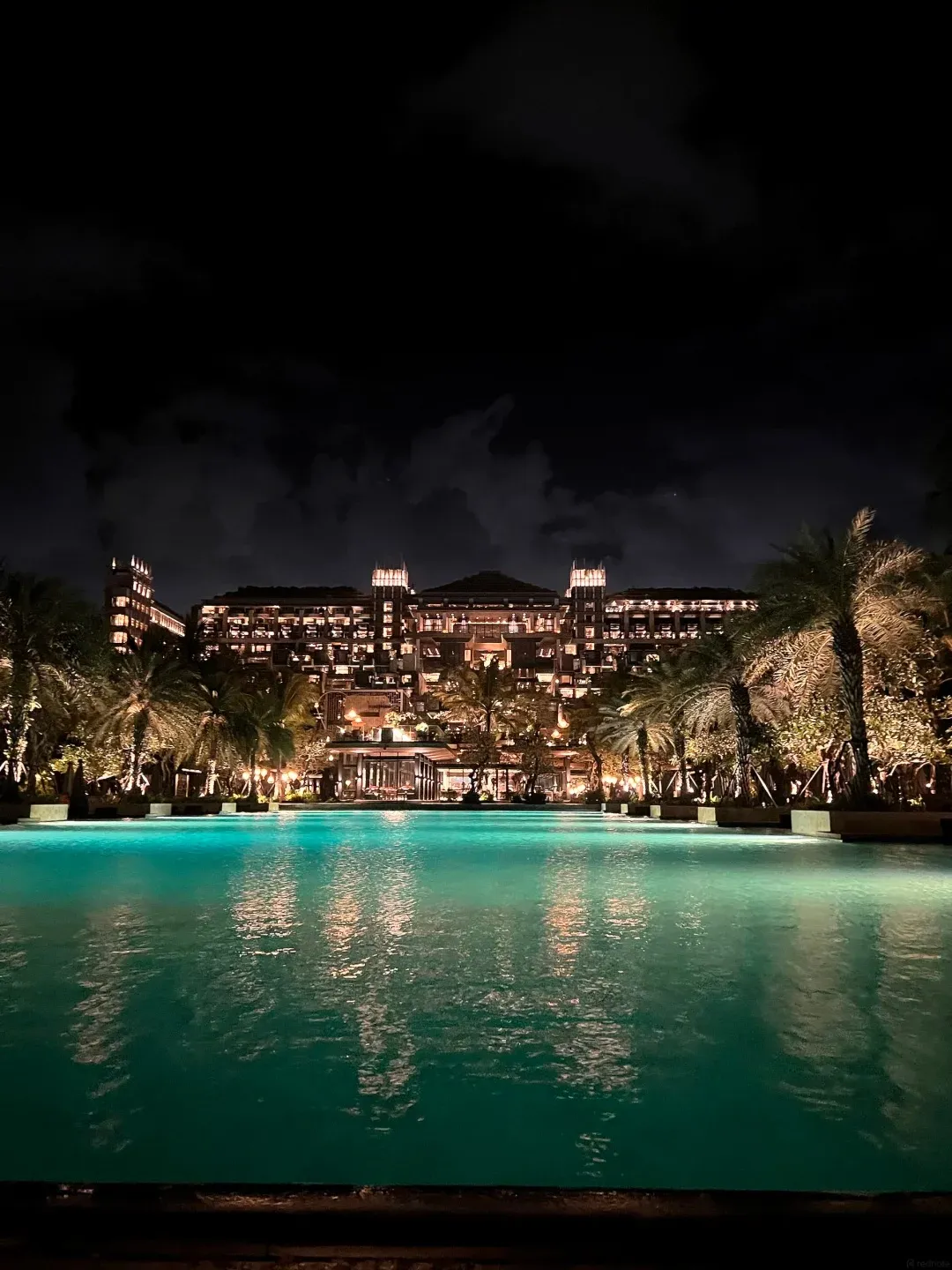 The resort lit up at night behind a long pool