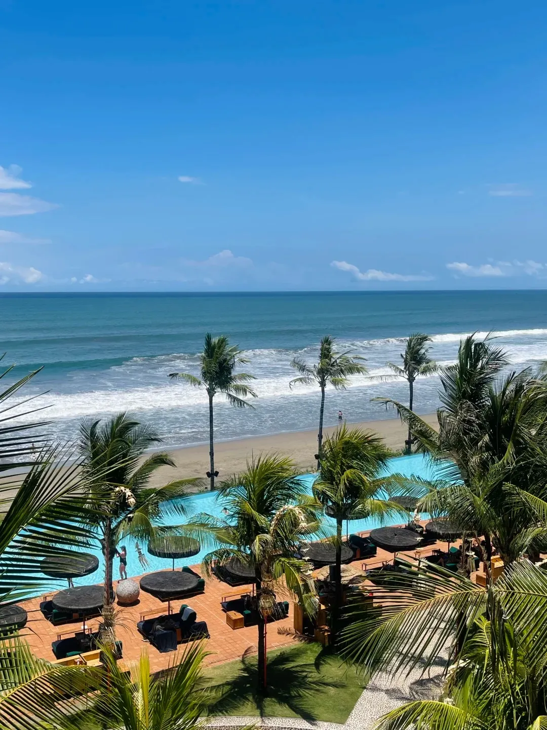 Looking down over the palms onto the pool, the umbrellas and the surf beyond