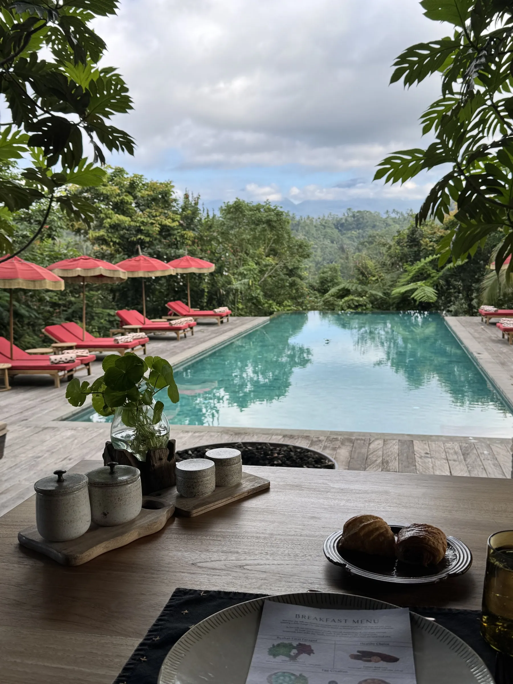 Breakfast at a table above the infinity pool, with red loungers and umbrellas and the valley beyond