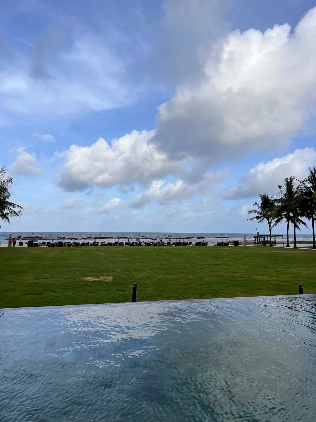 An infinity pool edge looking over a lawn to the sea