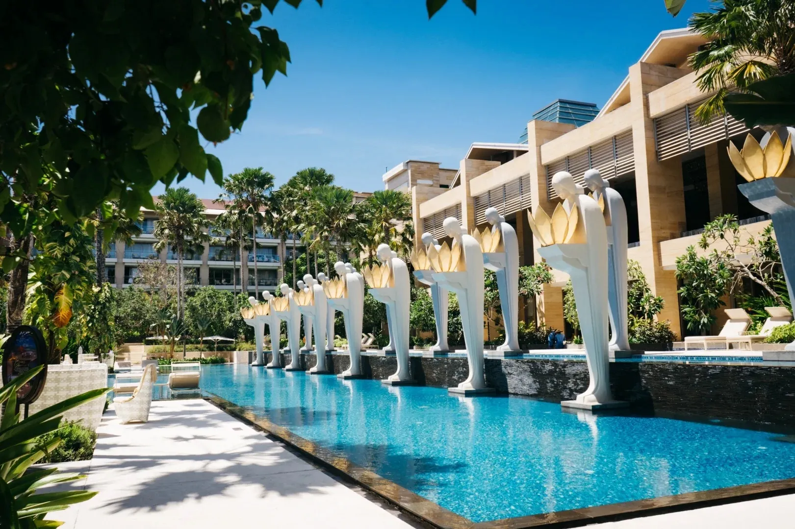 A row of white statues holding lamps along a long pool