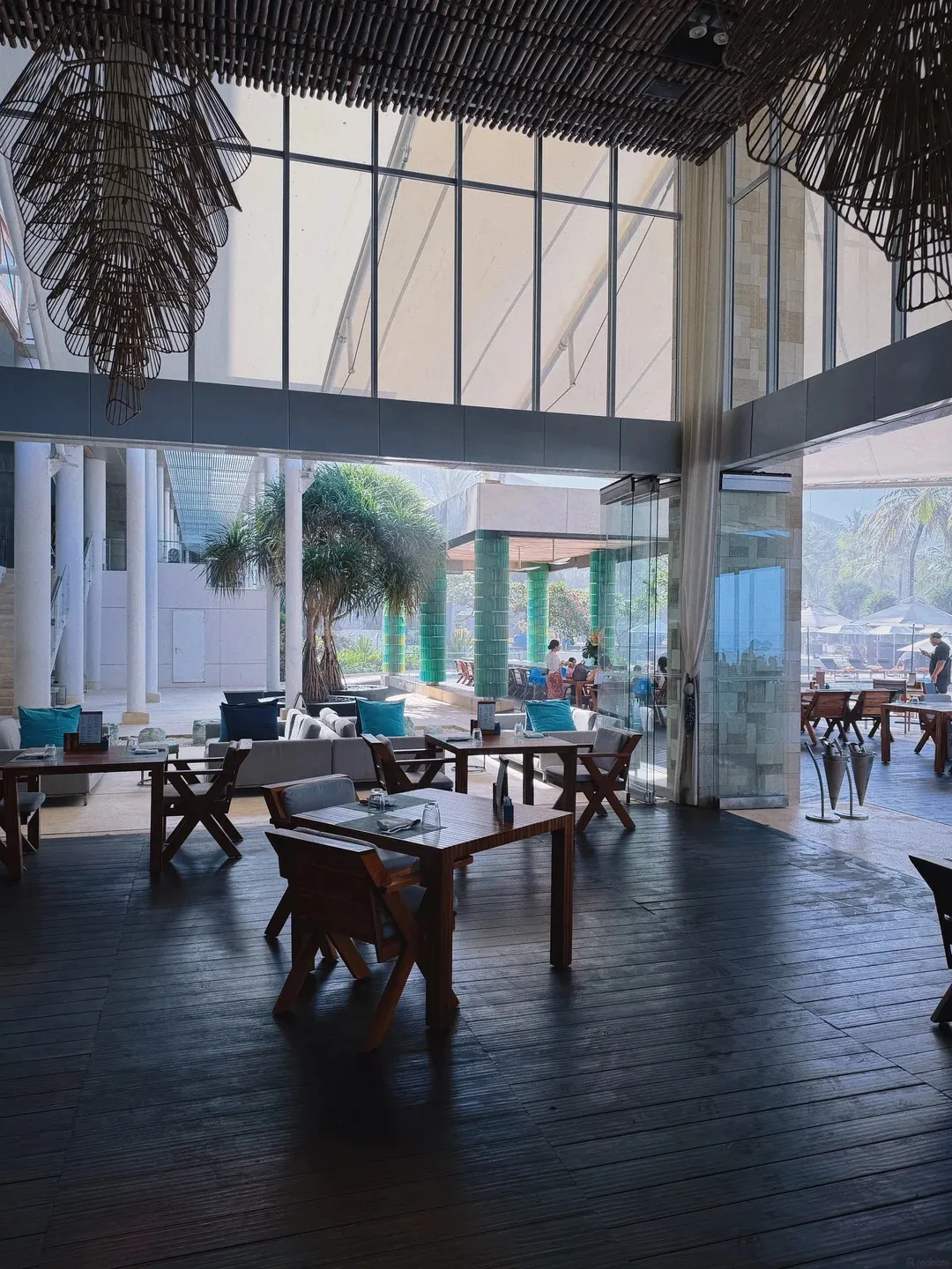 A double-height restaurant with timber tables and floor-to-ceiling glass onto the gardens