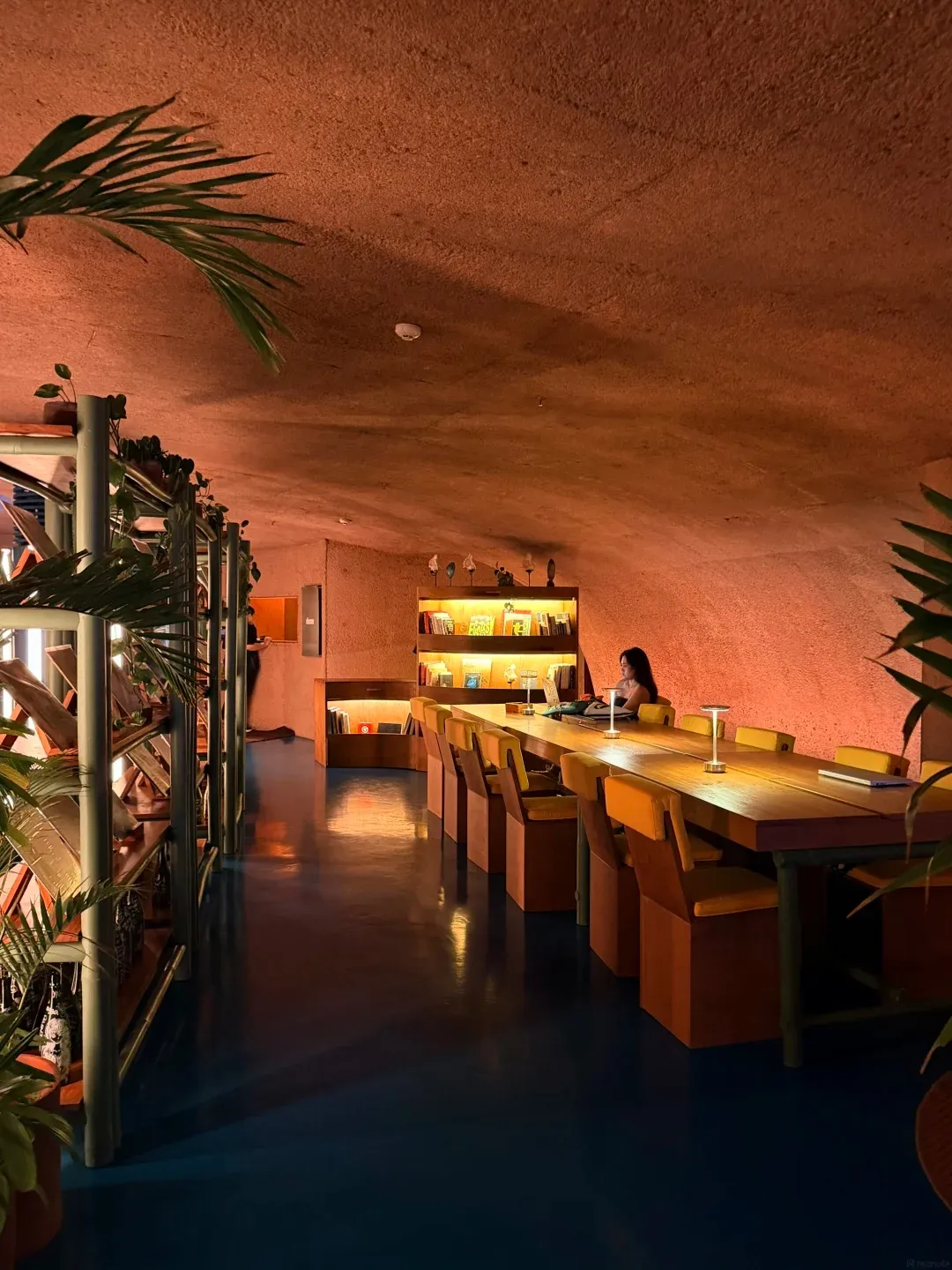 A long communal table in a glowing terracotta dining room with a curved ceiling