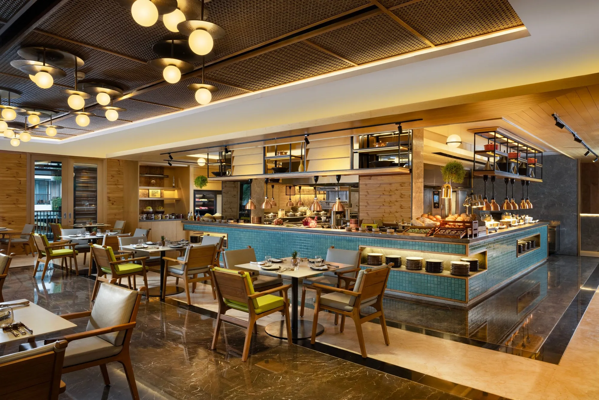 The restaurant’s open kitchen and buffet counter in blue tiles, with timber tables and globe lights