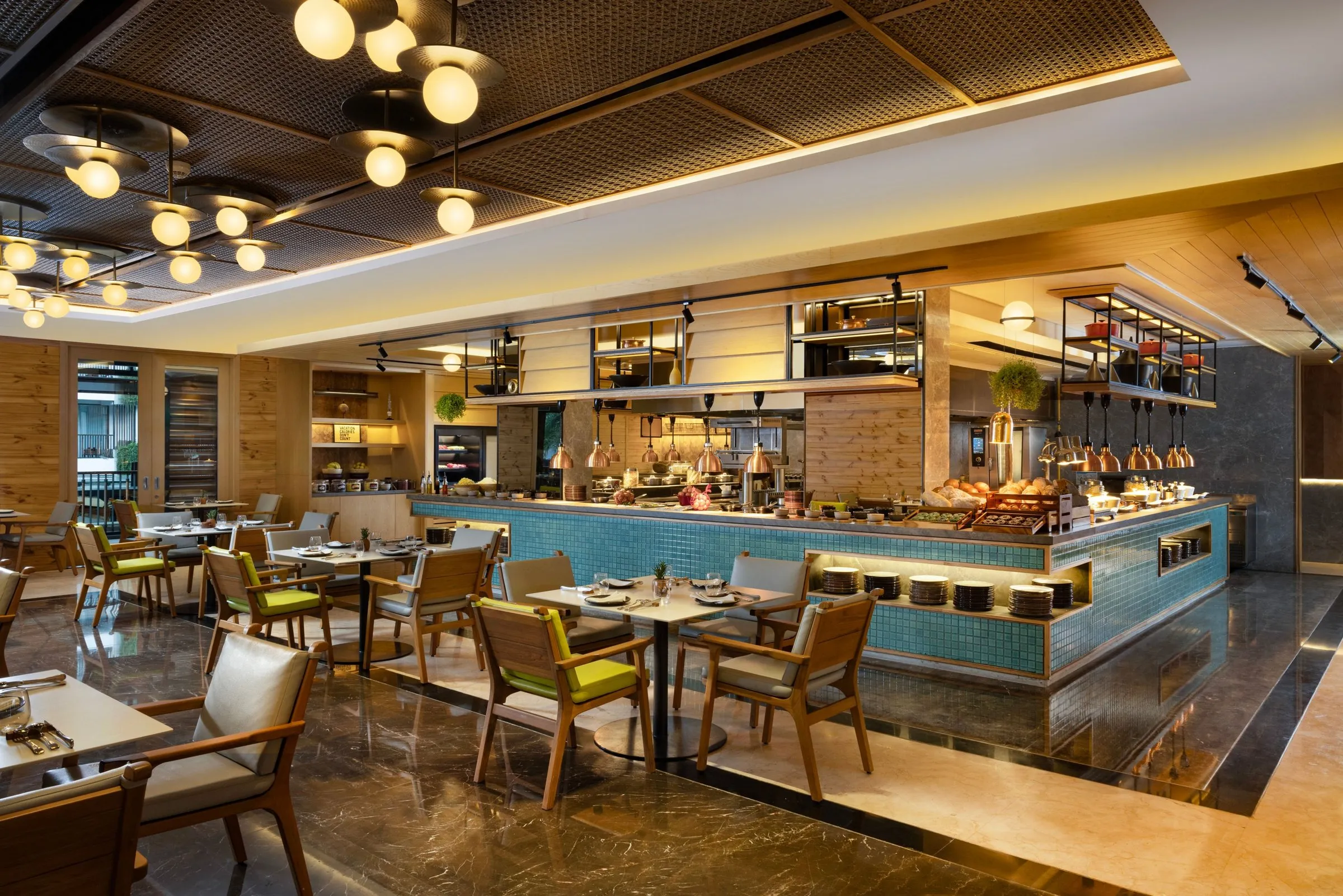 The restaurant’s open kitchen and buffet counter in blue tiles, with timber tables and globe lights