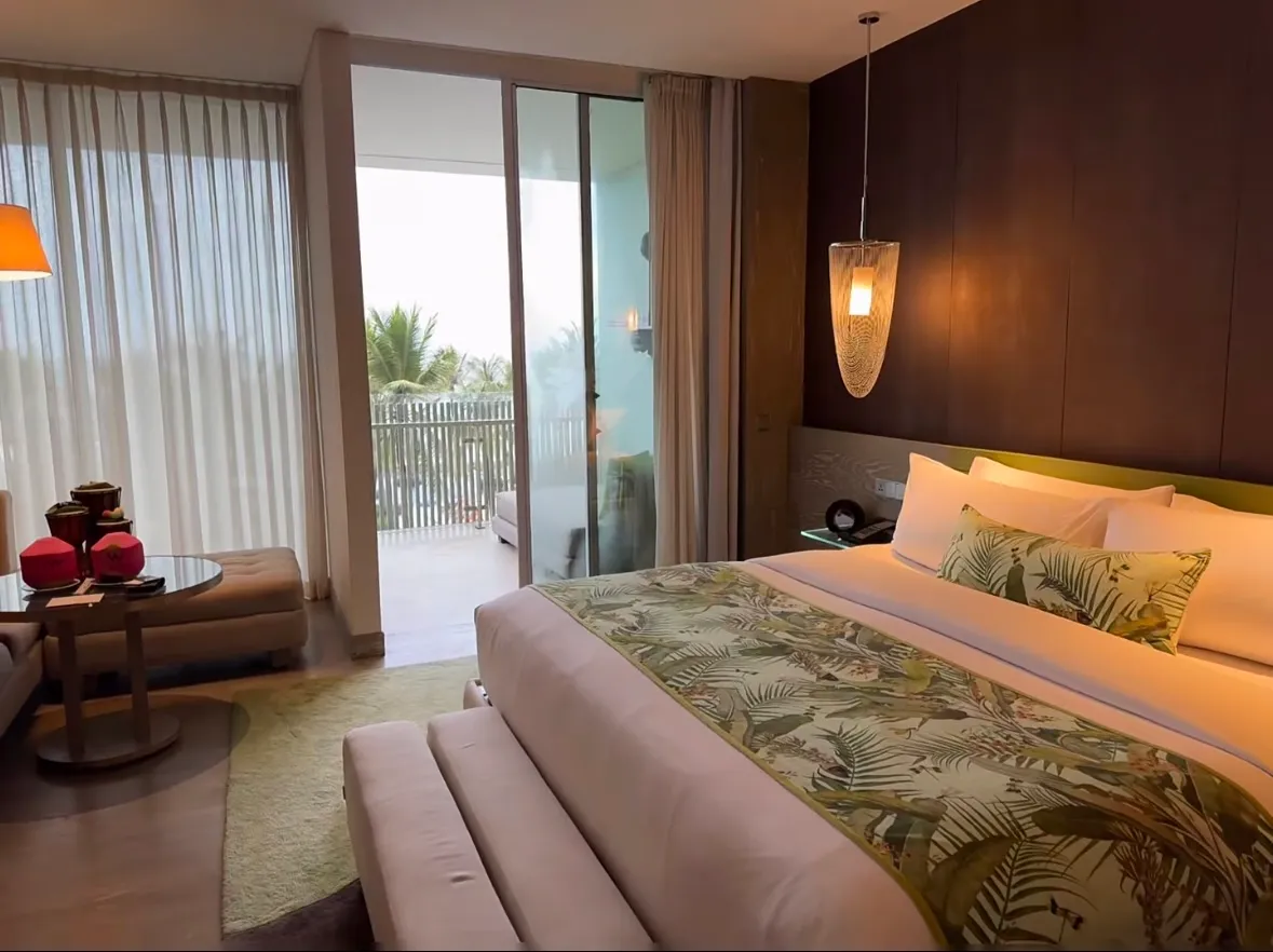 A W Bali room with a king bed under a palm-print runner, a pendant light and glass doors onto a balcony