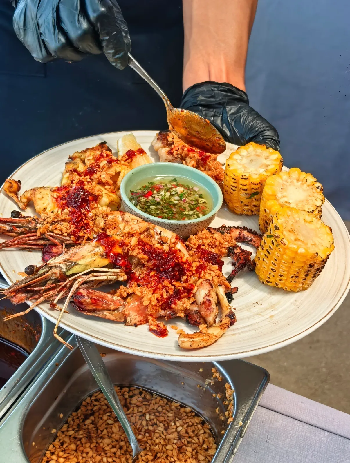 A chef spooning sambal over a grilled platter of king prawns, squid, octopus and charred corn