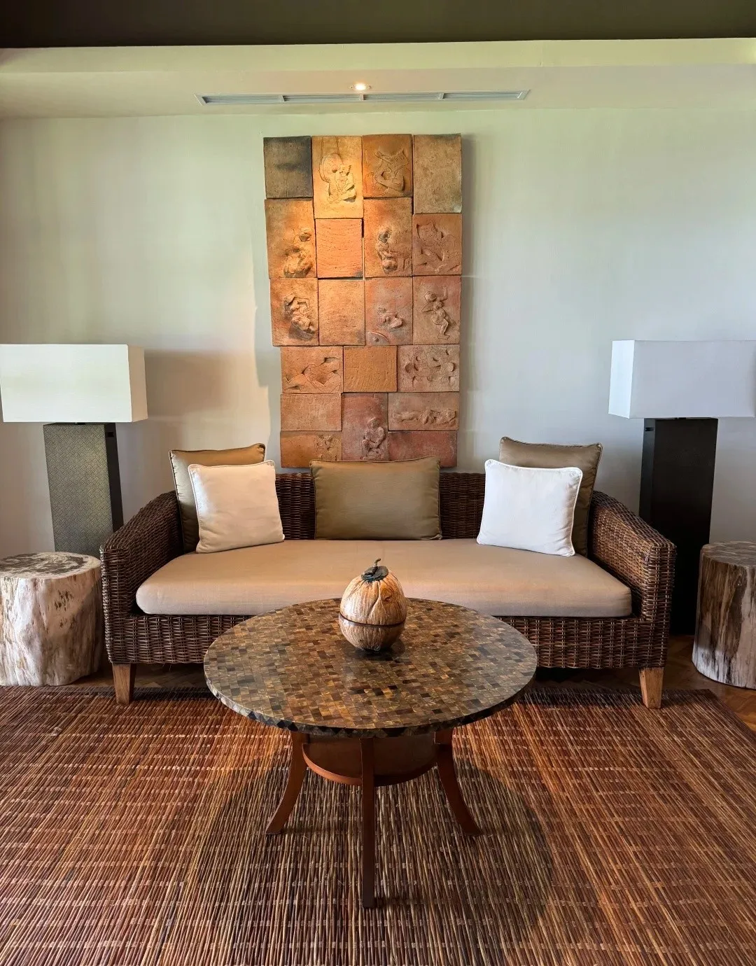 A suite lounge with a cream sofa, a round table on a woven rug and a carved stone panel on the wall