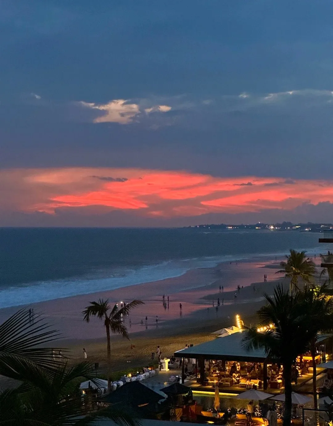 A red sunset over the beach, with the lights of the beach bar below