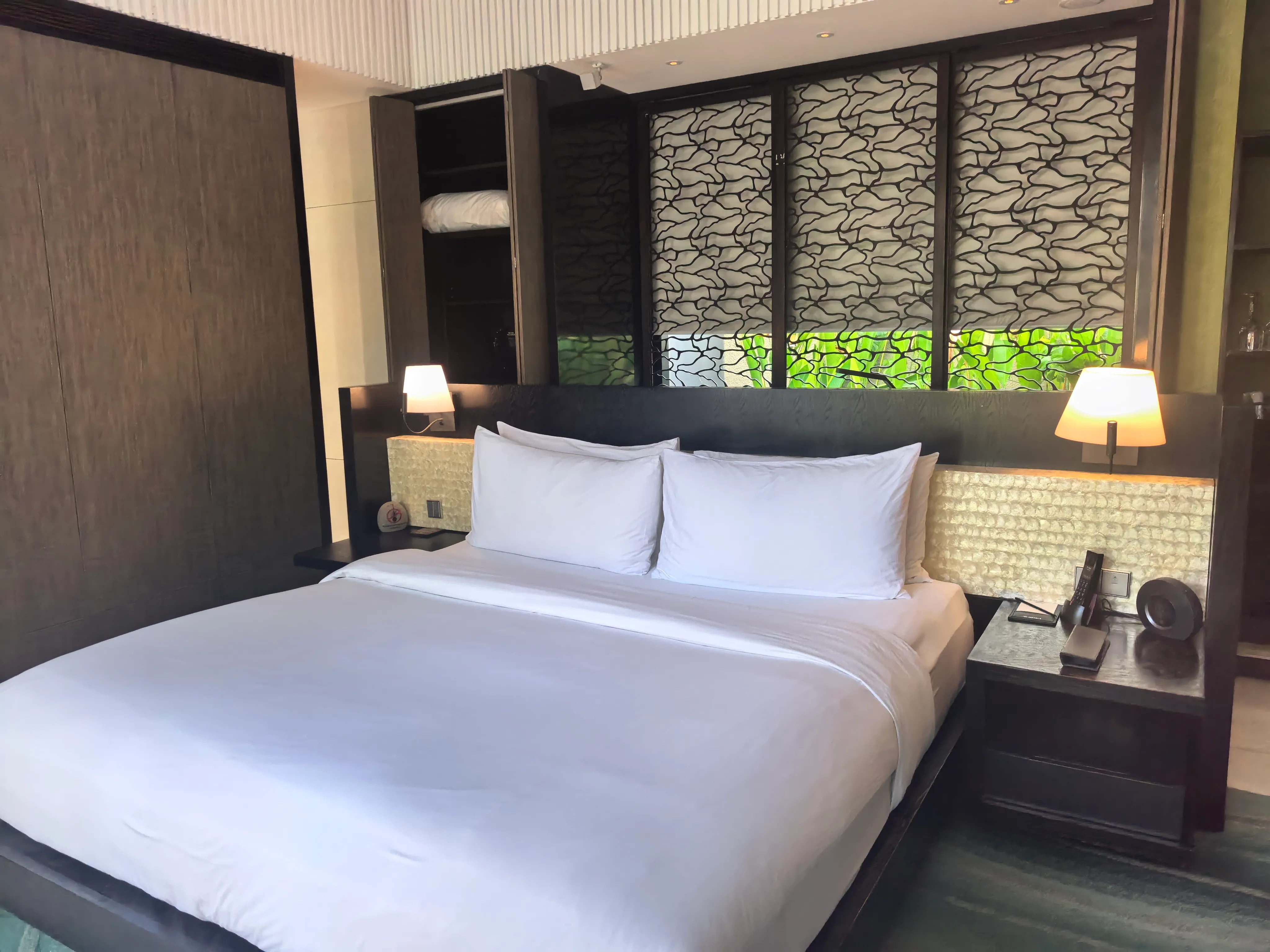 A villa bedroom with a king bed, a shell-inlay headboard and screened windows onto the garden