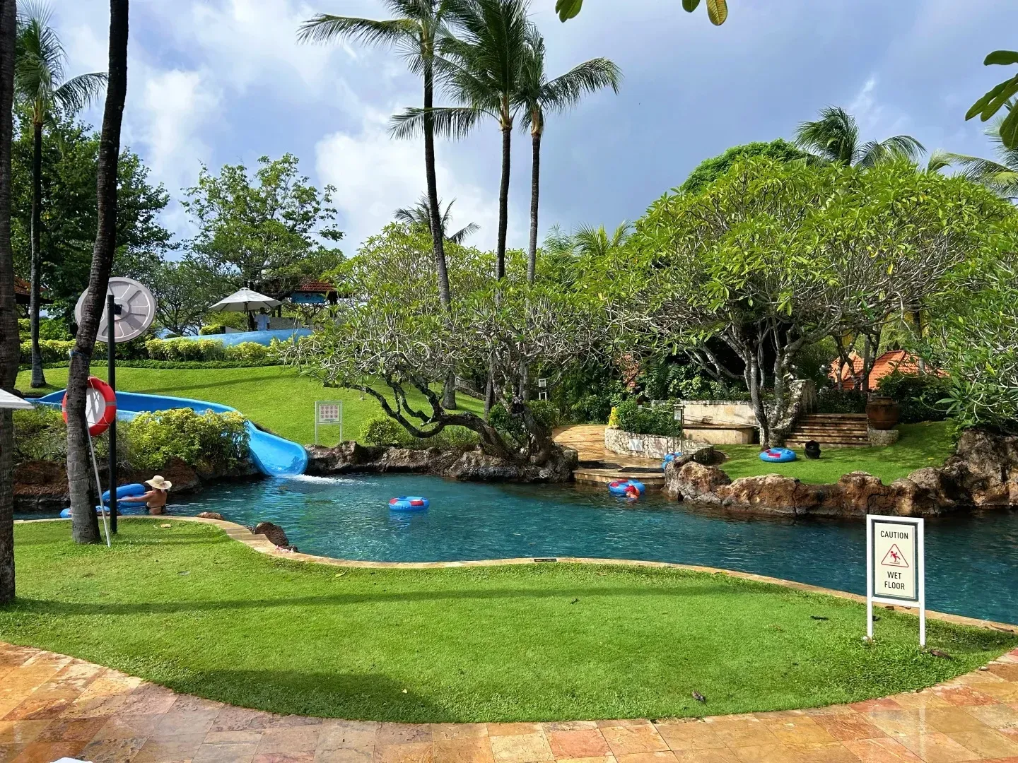 The waterslide splashing into a lagoon pool surrounded by lawn and frangipani trees